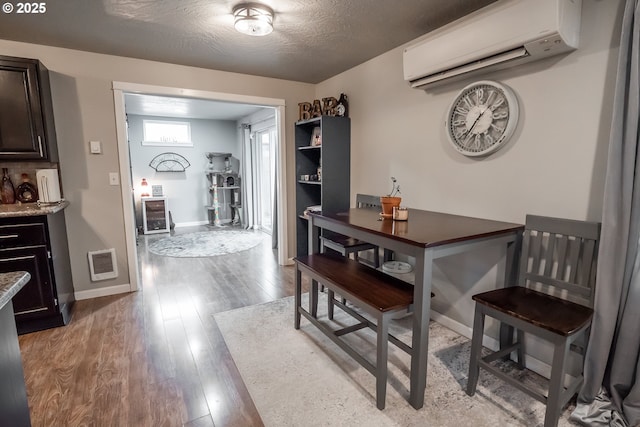 dining room with a textured ceiling, a wall unit AC, visible vents, baseboards, and light wood finished floors