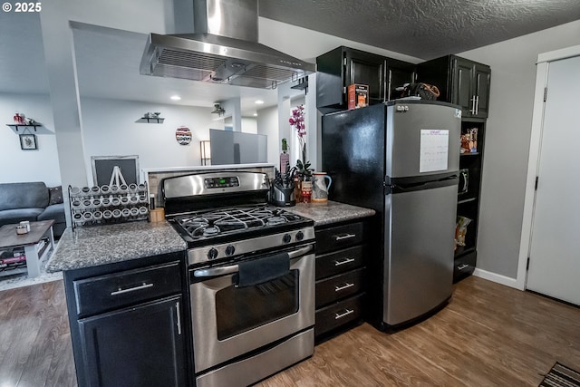 kitchen featuring a textured ceiling, wall chimney exhaust hood, appliances with stainless steel finishes, and wood finished floors