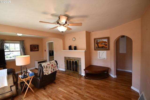 719 W 11th St, The Dalles, OR 97058 - living room featuring ceiling fan, arched walkways, baseboards, and a fireplace with flush hearth