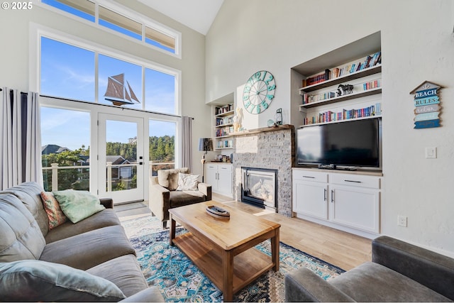 living room featuring a stone fireplace, built in shelves, light wood finished floors, and a towering ceiling