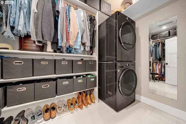 clothes washing area featuring laundry area, stacked washing maching and dryer, baseboards, and tile patterned flooring