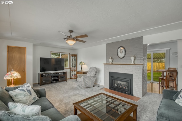 living room featuring a brick fireplace, carpet floors, a textured ceiling, and ceiling fan