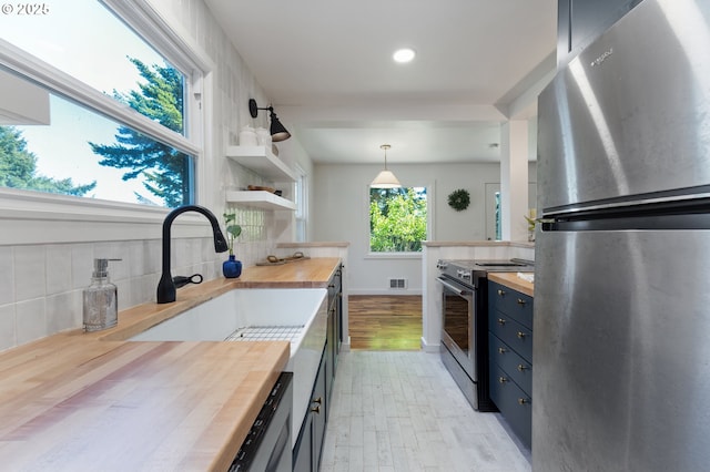 kitchen featuring visible vents, butcher block counters, stainless steel appliances, a sink, and blue cabinetry