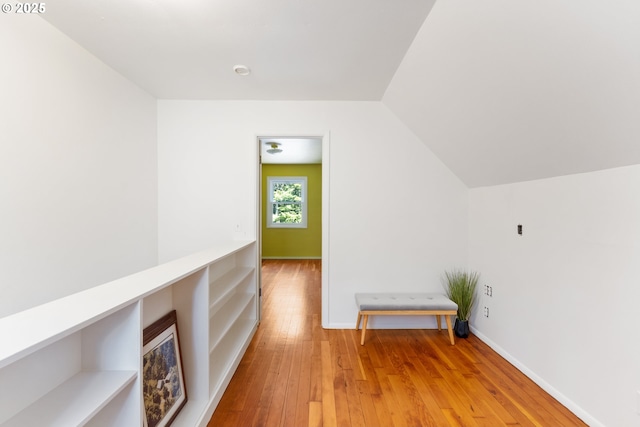 hall featuring baseboards, light wood finished floors, and lofted ceiling