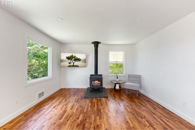 unfurnished room featuring visible vents, a wood stove, wood-type flooring, and baseboards