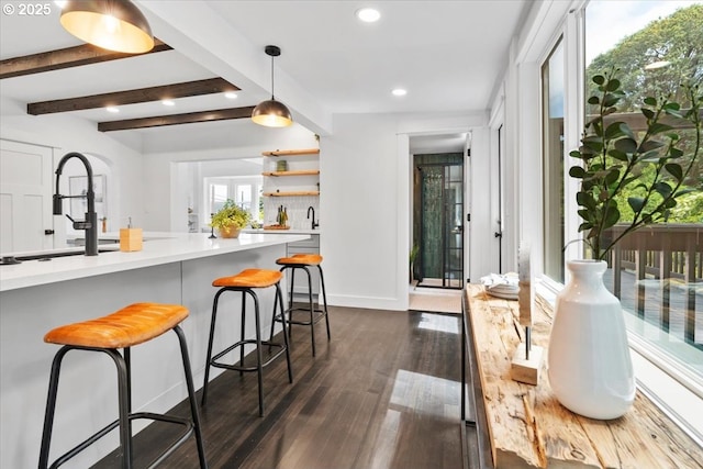 kitchen with decorative light fixtures, dark wood-type flooring, decorative backsplash, sink, and a breakfast bar