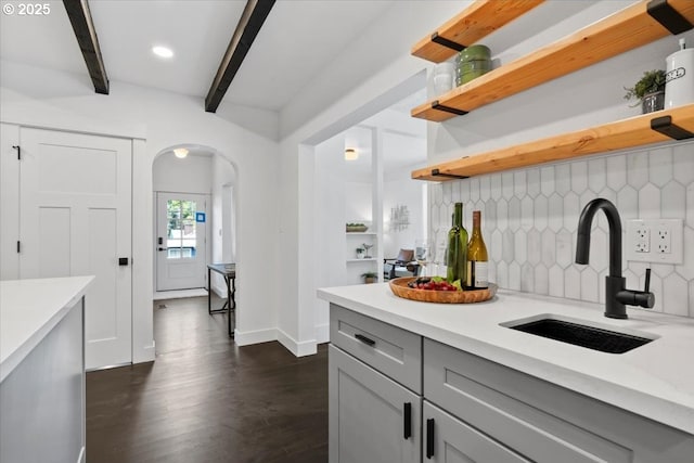 kitchen featuring sink, backsplash, gray cabinets, and beamed ceiling