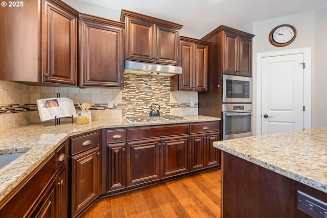 17007 NW Reuben Ln, Portland, OR 97229 - kitchen featuring stainless steel appliances, light wood-style floors, tasteful backsplash, under cabinet range hood, and light stone counters