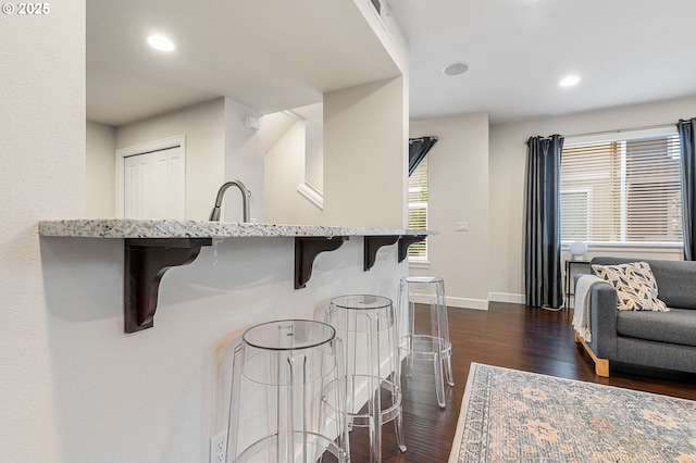 kitchen with light stone counters, a breakfast bar area, recessed lighting, dark wood-type flooring, and baseboards