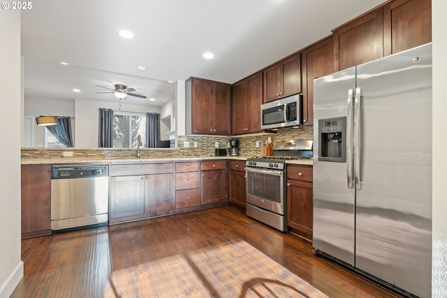 kitchen with dark wood-style flooring, decorative backsplash, appliances with stainless steel finishes, a sink, and light stone countertops