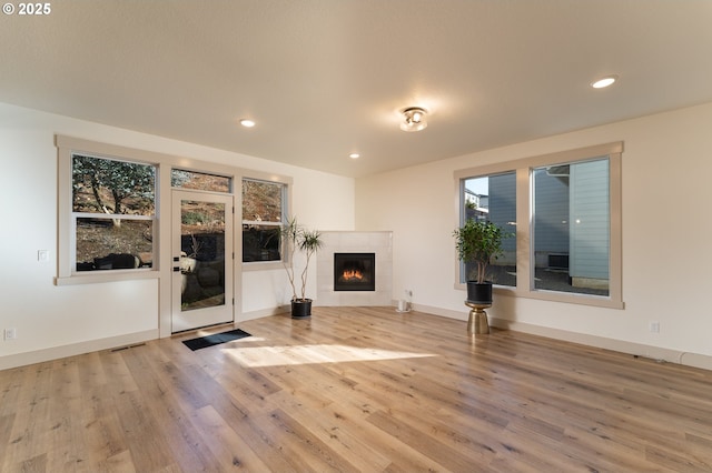 unfurnished living room with a tiled fireplace and light hardwood / wood-style floors