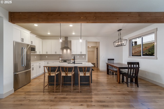 kitchen with wall chimney exhaust hood, appliances with stainless steel finishes, a kitchen island with sink, and white cabinets