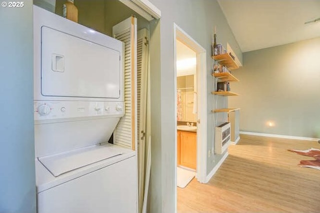 clothes washing area with light hardwood / wood-style floors, stacked washer / drying machine, and heating unit