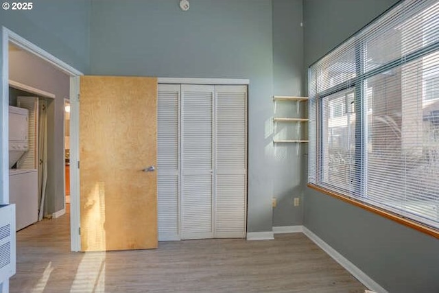 unfurnished bedroom with stacked washer and clothes dryer, a closet, and light hardwood / wood-style flooring