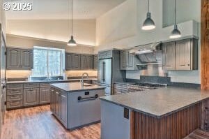 kitchen with a center island with sink, hanging light fixtures, gray cabinetry, light wood-style floors, and a peninsula