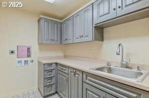 kitchen featuring baseboards, light countertops, a sink, and gray cabinetry