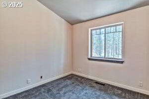 unfurnished room featuring dark colored carpet, visible vents, and baseboards