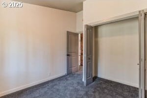 unfurnished bedroom with dark carpet and baseboards