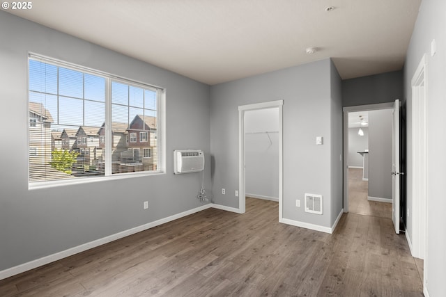 645 NW Falling Waters Ln Unit 303, Portland, OR 97229 - unfurnished bedroom with an AC wall unit, wood finished floors, a walk in closet, baseboards, and visible vents