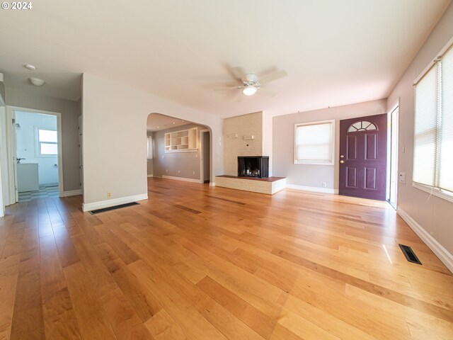 51055109 SE Tibbetts St, Portland, OR 97206 - unfurnished living room featuring a ceiling fan, light wood-type flooring, arched walkways, baseboards, and a brick fireplace