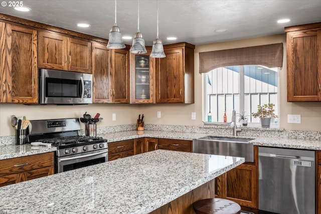 kitchen featuring stainless steel appliances, a sink, glass insert cabinets, hanging light fixtures, and light stone counters