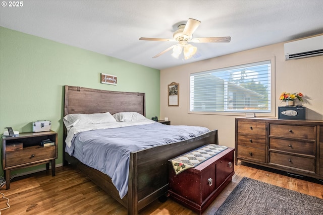 bedroom with a wall mounted AC, wood finished floors, and ceiling fan