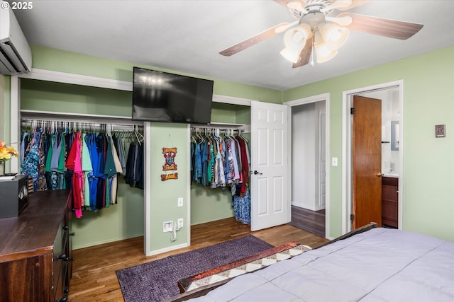 bedroom with wood finished floors, a wall mounted AC, baseboards, and ceiling fan