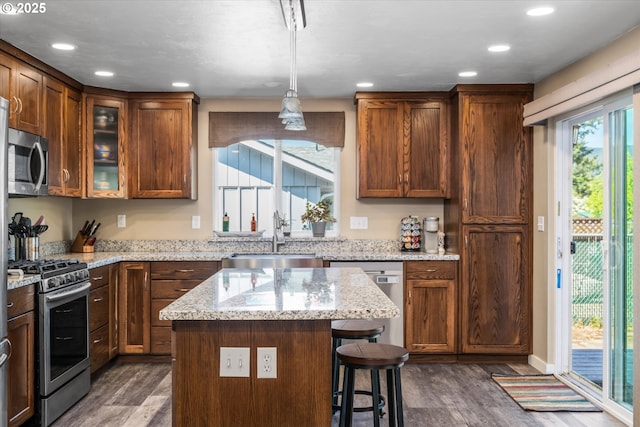 kitchen featuring appliances with stainless steel finishes, a sink, dark wood-style flooring, glass insert cabinets, and a breakfast bar