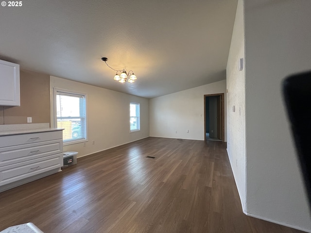 unfurnished living room with lofted ceiling, an inviting chandelier, visible vents, and dark wood finished floors