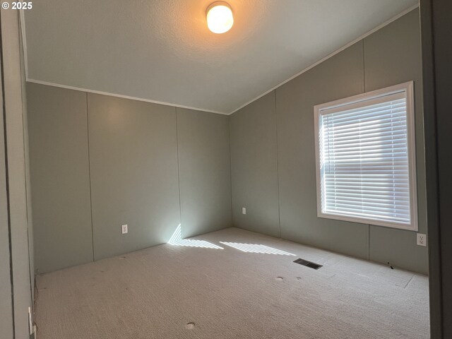 empty room featuring lofted ceiling, carpet flooring, visible vents, and crown molding