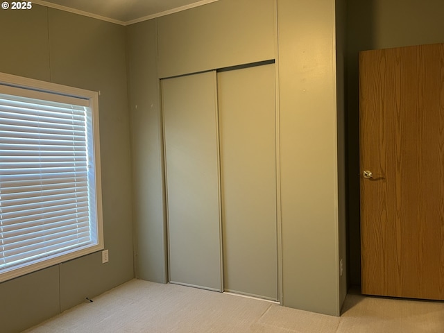 unfurnished bedroom with light carpet, multiple windows, ornamental molding, and a closet