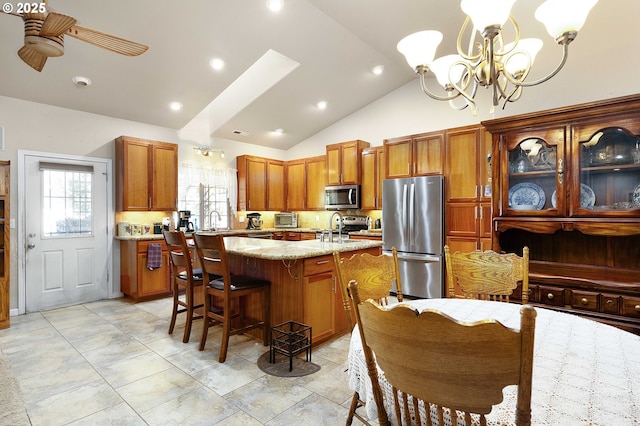 kitchen featuring light stone counters, a center island with sink, a breakfast bar, lofted ceiling, and stainless steel appliances