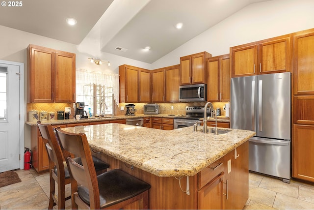 23164 N Umpqua Hwy, Idleyld Park, OR 97447 - kitchen featuring appliances with stainless steel finishes, lofted ceiling, a kitchen island with sink, light stone countertops, and decorative backsplash