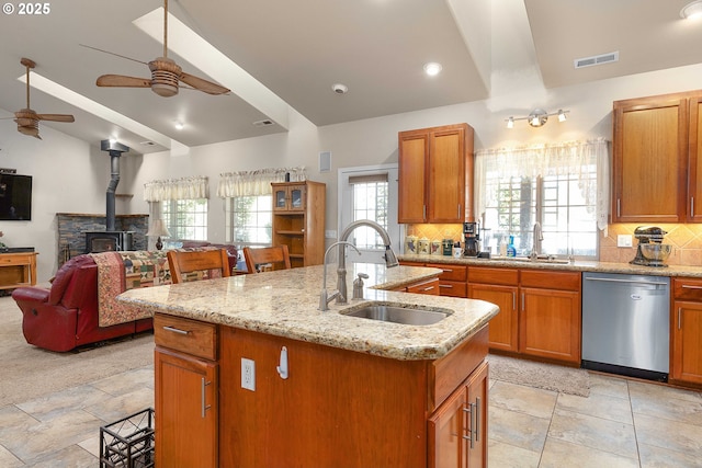 kitchen with visible vents, an island with sink, a sink, dishwasher, and a wood stove