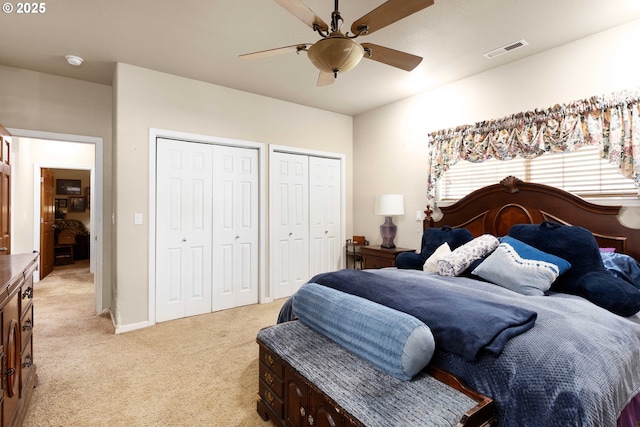 bedroom with visible vents, multiple closets, baseboards, light colored carpet, and ceiling fan