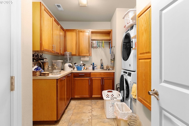 kitchen with visible vents, light countertops, brown cabinetry, stacked washer / drying machine, and a sink