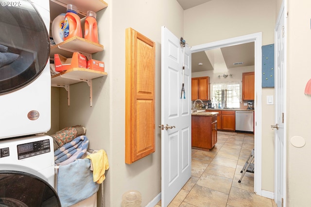 clothes washing area featuring a sink, baseboards, stacked washer and clothes dryer, and light tile patterned floors