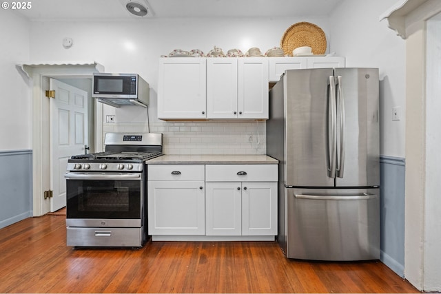 kitchen with stainless steel appliances, white cabinets, light countertops, tasteful backsplash, and dark wood-style flooring