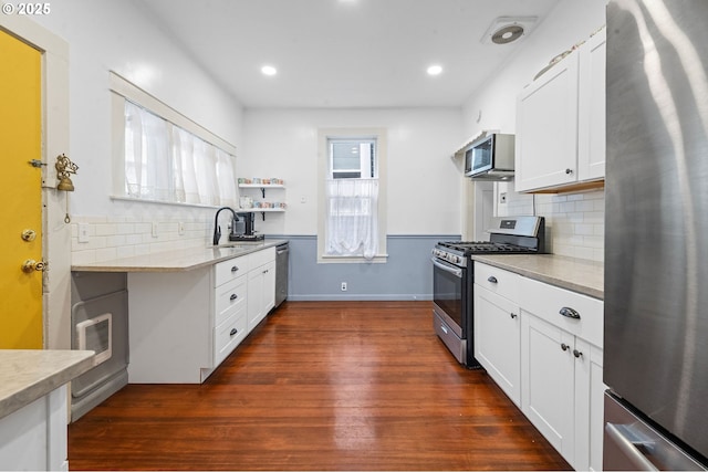 kitchen with stainless steel appliances, a sink, dark wood-style flooring, decorative backsplash, and white cabinetry