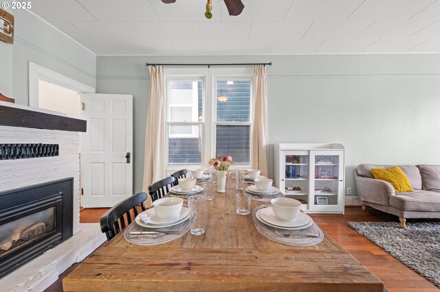 dining space featuring wood finished floors, a glass covered fireplace, and ceiling fan