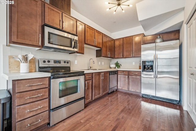 680 NW Falling Waters Ln Unit 105, Portland, OR 97229 - kitchen with appliances with stainless steel finishes, dark wood-type flooring, tasteful backsplash, a chandelier, and brown cabinets
