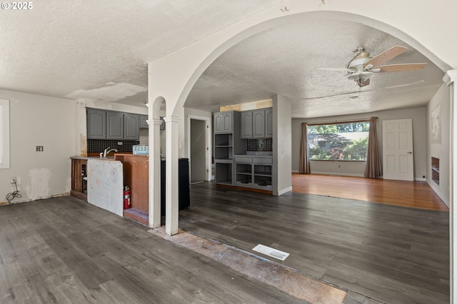 1203 NE 190th Pl, Portland, OR 97230 - unfurnished living room featuring a textured ceiling, arched walkways, a ceiling fan, dark wood finished floors, and ornate columns