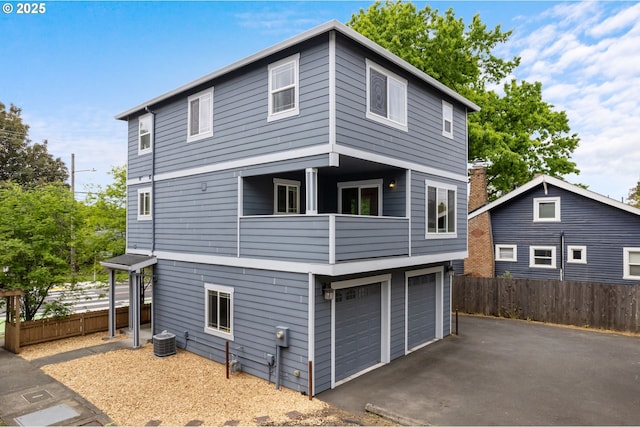 back of property with fence, central AC unit, a balcony, and an attached garage