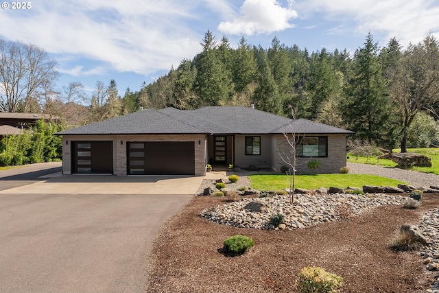 view of front of house with aphalt driveway, roof with shingles, brick siding, a front yard, and a garage