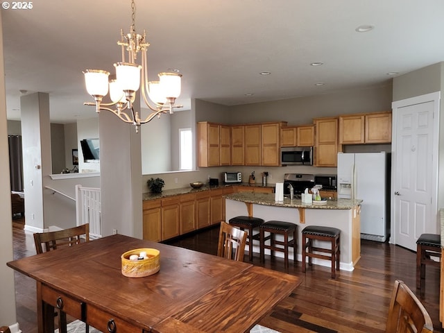 kitchen with stainless steel appliances, a notable chandelier, dark hardwood / wood-style flooring, a kitchen island, and light stone counters