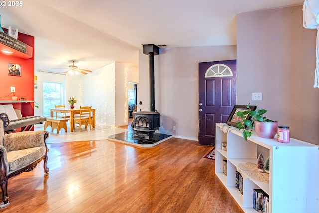 foyer entrance featuring ceiling fan, wood finished floors, and a wood stove