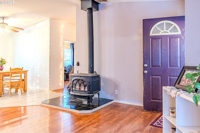 foyer with a wood stove, ceiling fan, baseboards, and wood finished floors