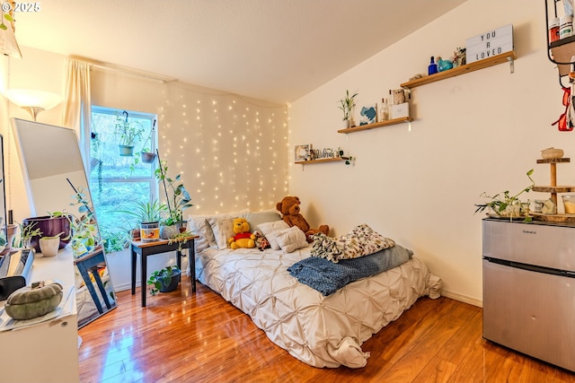 bedroom featuring baseboards, wood finished floors, and refrigerator