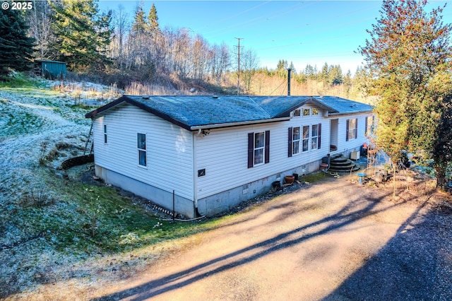 view of side of property featuring dirt driveway, roof with shingles, and crawl space