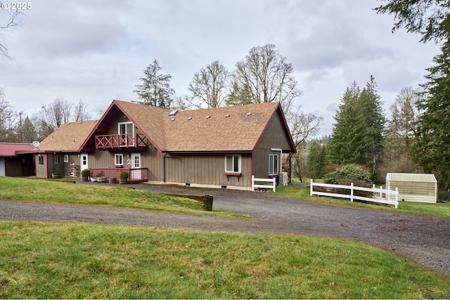 view of front of property with aphalt driveway, a balcony, a shingled roof, fence, and a front yard